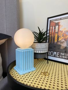 a lamp sitting on top of a table next to a potted plant and a poster