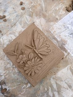 a clay sculpture of a dragonfly and flowers on a piece of tin foil with rocks in the background