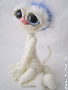 a crocheted stuffed animal with big eyes and blue hair sitting on a white surface