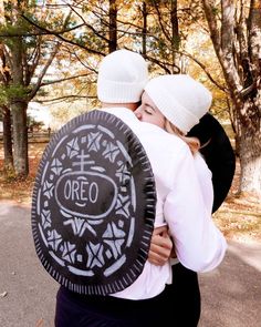 two people hug each other while holding an oreo cookie in front of trees and leaves