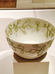 a white bowl sitting on top of a table next to a glass case filled with flowers