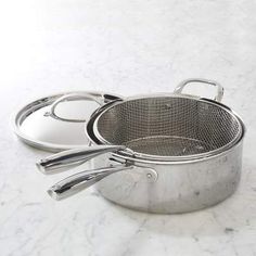 two stainless steel pots and pans sitting on a marble counter top with one holding a spatula