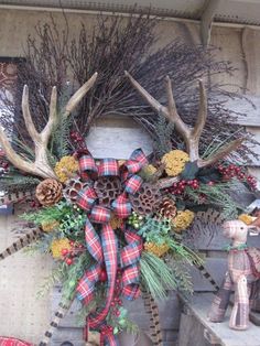 a wreath with antlers, pine cones and plaid ribbon hanging on the front door