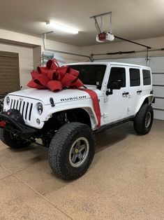 a white jeep with a large red bow on it's hood parked in a garage