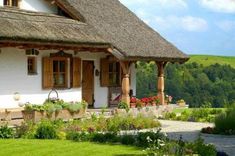 a small white house with a thatched roof and flowers in the front garden area