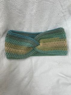 a crocheted headband laying on top of a white sheet with green and yellow stripes