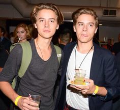 two young men standing next to each other holding drinks