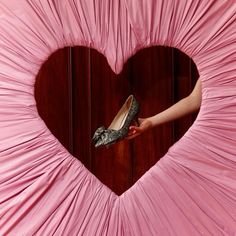 a woman's hand holding a pair of shoes in front of a pink heart