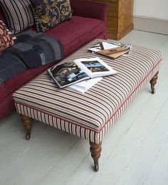 a striped ottoman sitting on top of a white floor next to a red couch and wooden coffee table