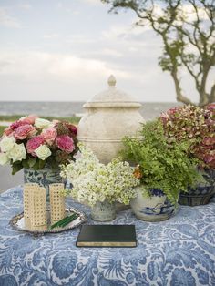 a table topped with vases filled with flowers and greenery next to a stone urn