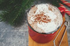 a cup of hot chocolate with whipped cream and cinnamon on the side next to a candy cane