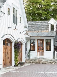 a white house with two brown doors and brick walkway leading up to the front door