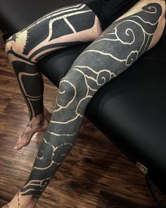 a man sitting on top of a black couch covered in tattoos and leggings