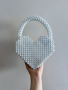 a hand holding a white beaded purse on top of a gray wall next to a grey wall