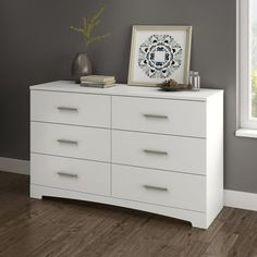 a white dresser sitting in front of a window with a vase on top of it