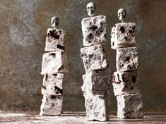 three skulls sitting on top of blocks of rock with one skull in the middle and two smaller ones standing behind them