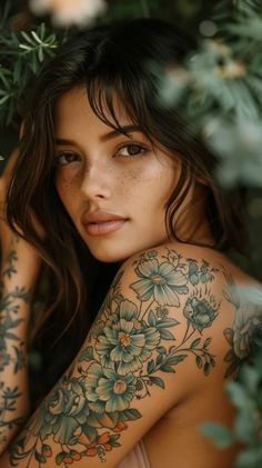 a beautiful woman with tattoos on her arm and chest posing in front of some flowers