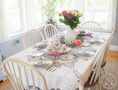 a dining room table is set with plates and flowers in a vase on the table