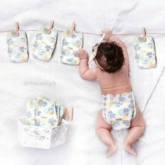 a baby laying on top of a white bed next to clothes hanging from a line