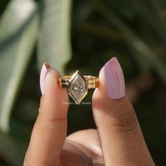 a woman's hand holding an engagement ring in front of her face with the diamond on it