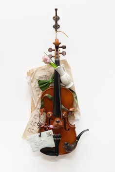 a clay, paper, and resin sculpture of a violin with a dog's face on the front, hanging from a hook with a plant and some written music