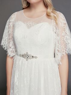 a woman wearing a white wedding dress with sheer sleeves and a beaded waist belt