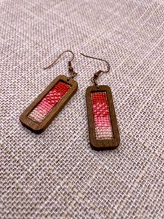 two wooden earrings with red and white designs on them sitting on a piece of fabric