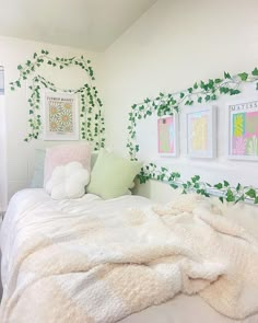 a bedroom with white bedding and green plants on the wall above it, along with pictures hanging on the wall