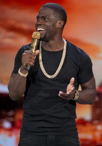 a man holding a microphone in his right hand and wearing a chain around his neck