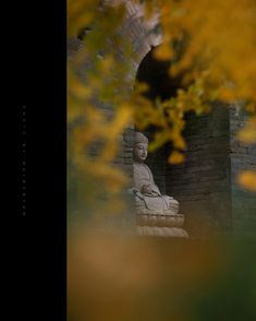 a buddha statue sitting in the middle of a brick wall with yellow flowers around it