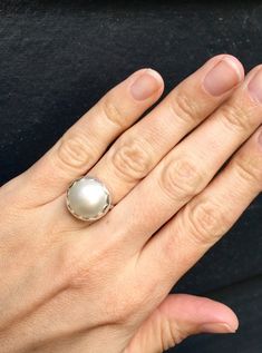 Choose your color and your ring size! This elegant and stately pearl ring is made from a beautiful and unique white cream 14mm Mabe South Sea AAA Pearl that has many hues including pink. The pearl has been set in sterling silver with a sterling silver ring band handmade from half dome wire. This ring has some height, the setting is almost 1/2 inch high. The white cream pearl is more matte than the other mabe pearls listed, but still has a luminescent quality that makes it captivating!Made to ord Elegant Sterling Silver Cabochon Pearl Ring, Classic White Pearl Ring With Drop Detail, Elegant Round Cabochon Pearl Ring, Elegant Oval Pearl Ring With Bezel Setting, Elegant White Pearl Ring With Round Band, Elegant White Pearl Ring, Elegant White Adjustable Moonstone Ring, Classic White Pearl Ring With Pearl Charm, Classic White Pearl Ring With Charm