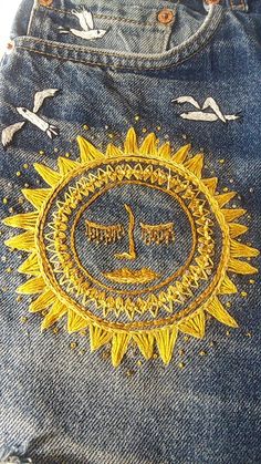 a pair of jeans with embroidered sun and birds on them