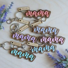 six keychains with names on them sitting next to purple flowers and greenery