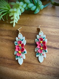 two pairs of earrings with flowers on them sitting on a table next to some plants