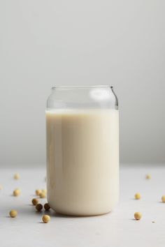 a glass jar filled with milk sitting on top of a white table next to some chickpeas