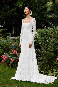 a woman standing in front of flowers wearing a white wedding dress with long sleeves and an open back