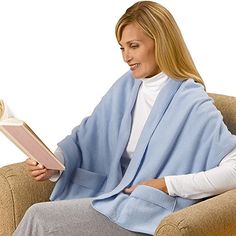 a woman is sitting in a chair and reading a book while wearing a blue blanket