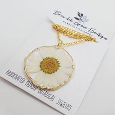 a white and yellow flower is on a gold plated chain with a tag attached to it