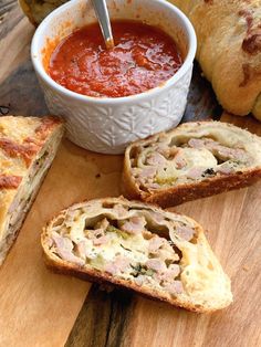 bread with meat and tomato sauce on it sitting on a cutting board next to rolls