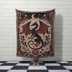 a woman standing in front of a black and white checkered floor holding a tapestry with a dragon on it