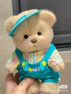 a small teddy bear wearing overalls and a hat is being held by someone's hand