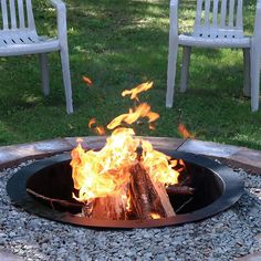 a fire pit sitting on top of a gravel field next to white chairs and grass