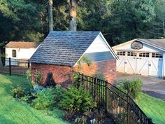 a brick house with a black fence and trees in the backgroung area