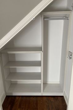 an empty closet in the corner of a room with wooden floors and white walls, under a slanted roof