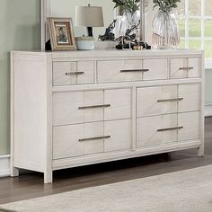 a white dresser with two vases on top of it next to a mirror and lamp