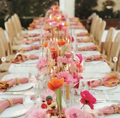 a long table is set with pink and orange flowers in vases, candles and napkins