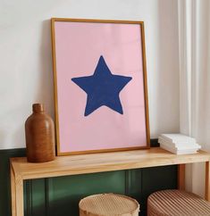 a framed blue star on a pink background next to two wicker stools and a wooden table