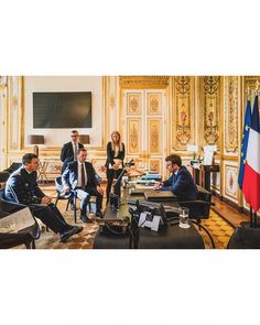 a group of people sitting around a table in a room with flags on the walls