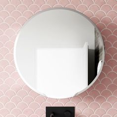 a round mirror mounted to the side of a pink wall next to a black hook