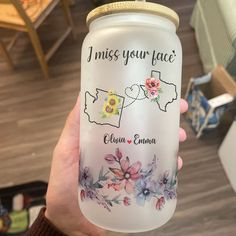 a person holding up a personalized mason jar with flowers and state names on it